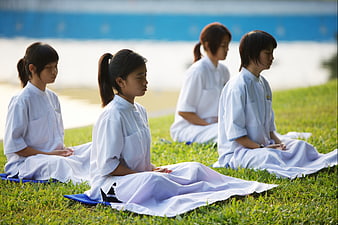 Young Buddhist girls meditating in white robes on a grassy field