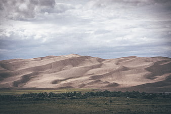 Vast sand dunes landscape with green valley and cloudy sky