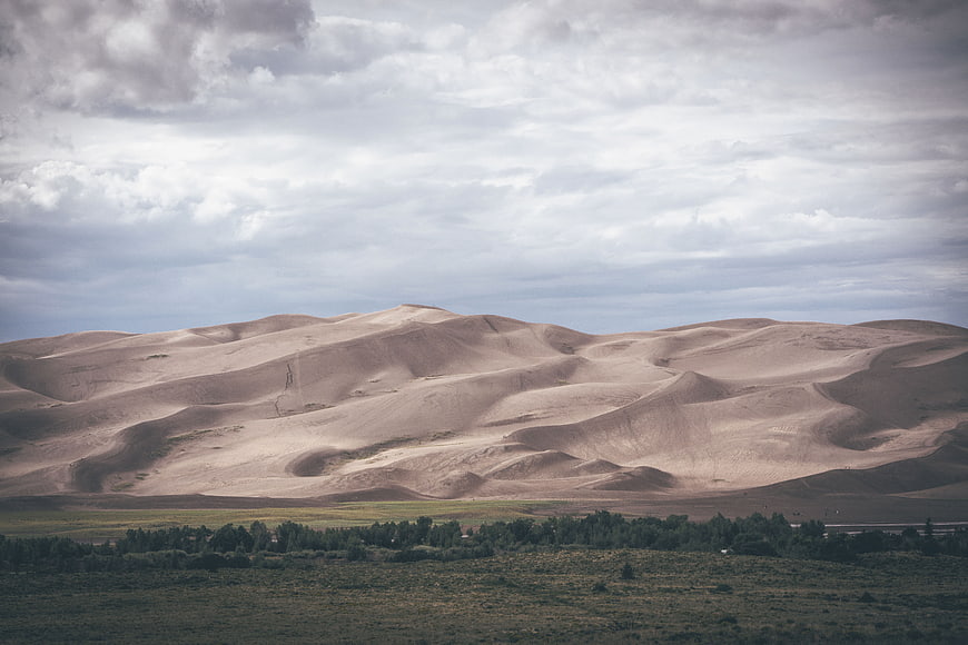 Vast sand dunes landscape with green valley and cloudy sky