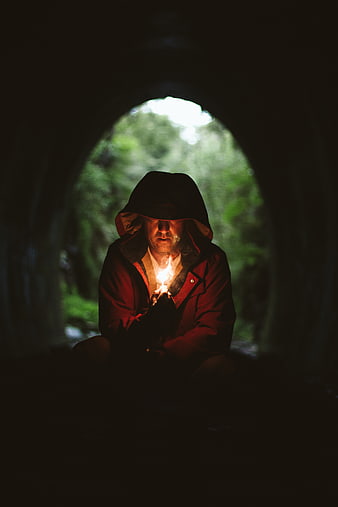 Man in Hooded Jacket Holding Fire in Dark Tunnel