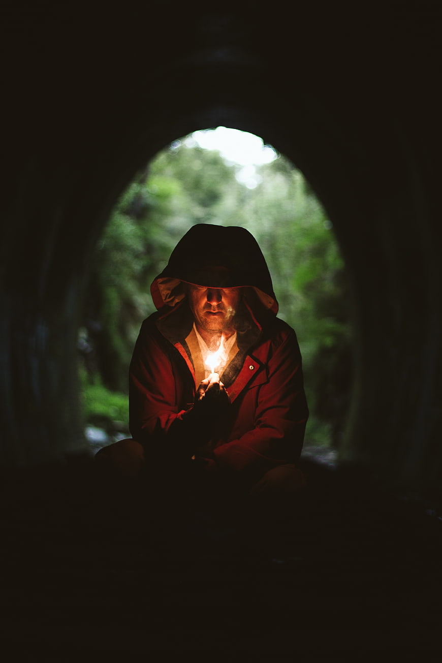 Man in Hooded Jacket Holding Fire in Dark Tunnel