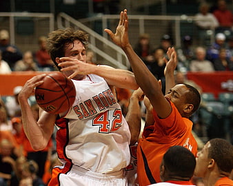 College basketball player in white jersey holding ball against defender