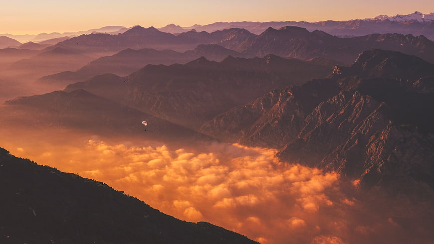 Paraglider soaring above golden sunset clouds in mountain range