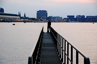 Silhouette of person on pier overlooking city skyline at dusk