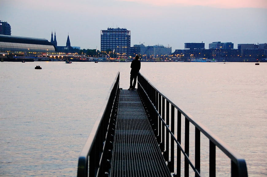 Silhouette of person on pier overlooking city skyline at dusk