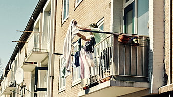 Woman Hanging Laundry on Apartment Balcony