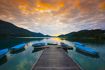 Blue boats docked at wooden pier on lake at sunset
