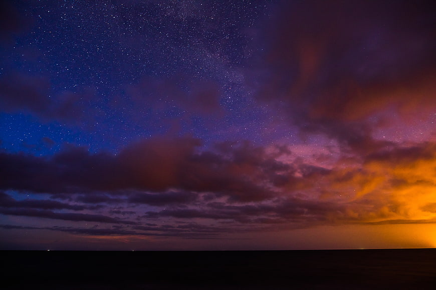 Dramatic Starry Night Sky with Colorful Clouds and Horizon