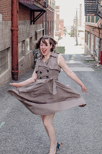 Joyful woman twirling in brown dress in urban alley