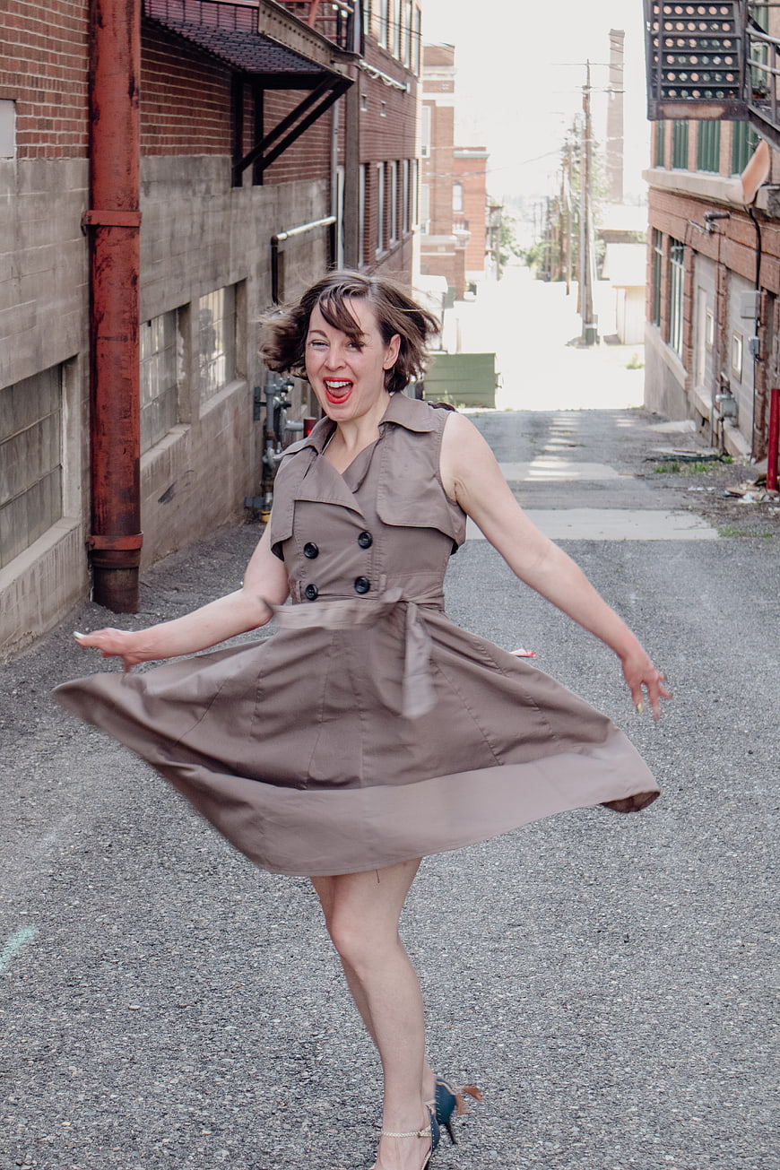 Joyful woman twirling in brown dress in urban alley