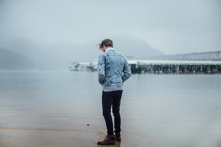 Man in Denim Jacket Standing on Foggy Beach Shore