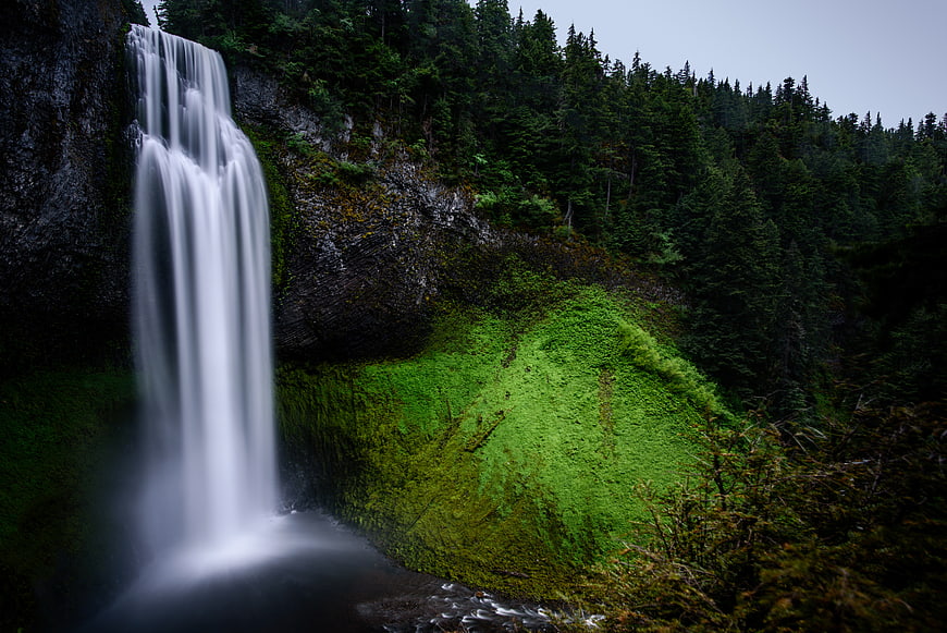 Misty waterfall cascading down mossy cliff in dark forest