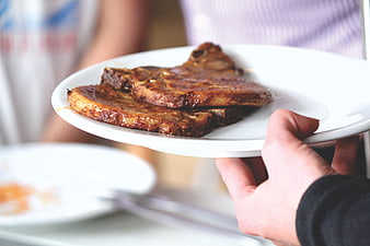 Hand holding plate of grilled pork ribs