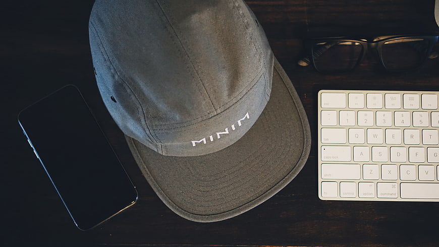 Flat lay of grey cap, smartphone, keyboard, and glasses on desk