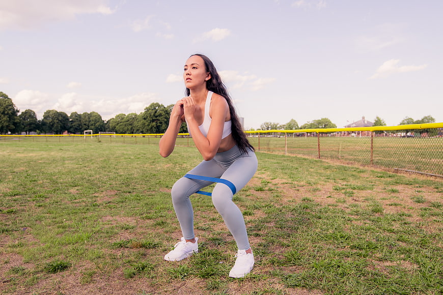 Woman doing resistance band squat workout outdoors