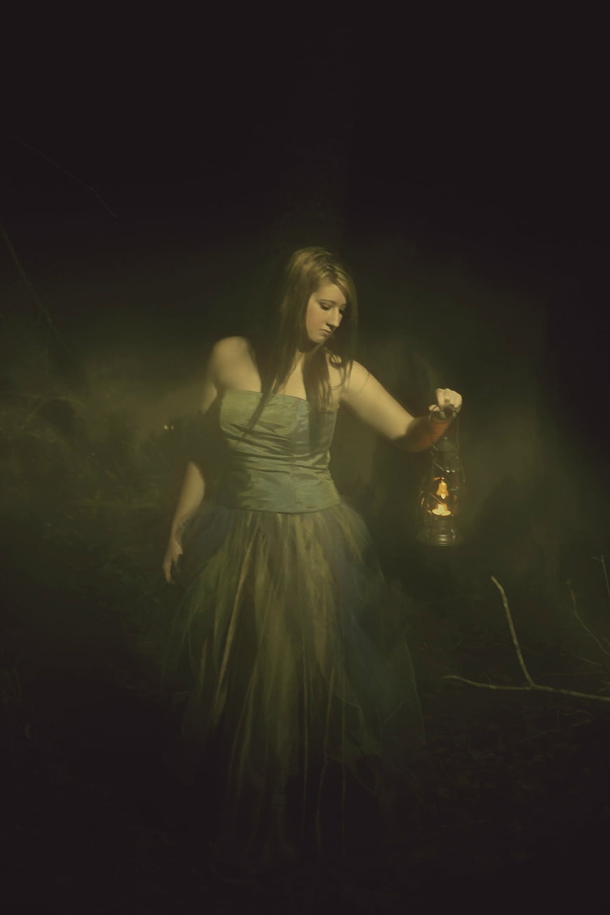 Woman in Green Dress Holding Lantern in Dark Forest