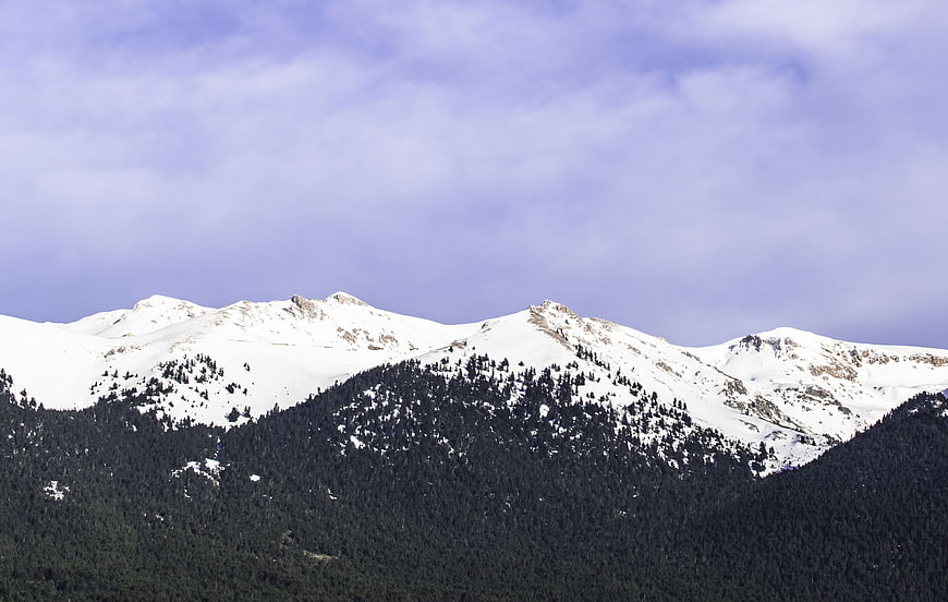 Snow-Capped Mountain Peaks with Forested Slopes and Cloudy Sky