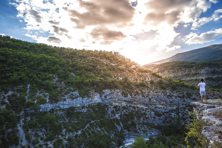 Man Standing on Cliff Edge Overlooking Mountain Valley