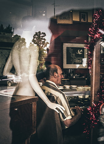 Senior man sitting in shop window with mannequin reflection