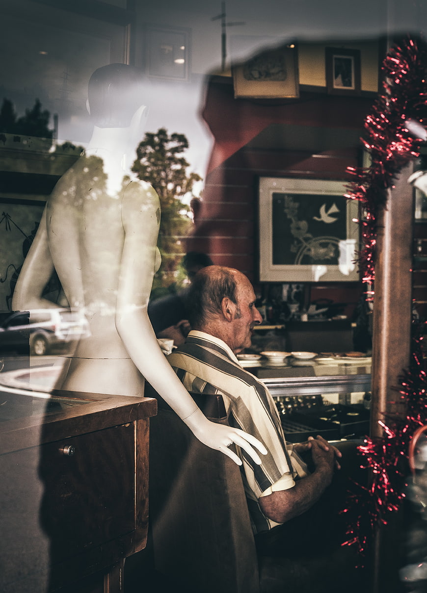 Senior man sitting in shop window with mannequin reflection