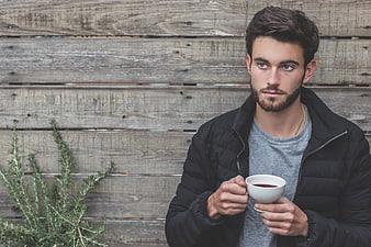 Young man with beard holding coffee cup against rustic wood wall
