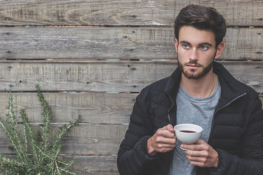 Young man with beard holding coffee cup against rustic wood wall