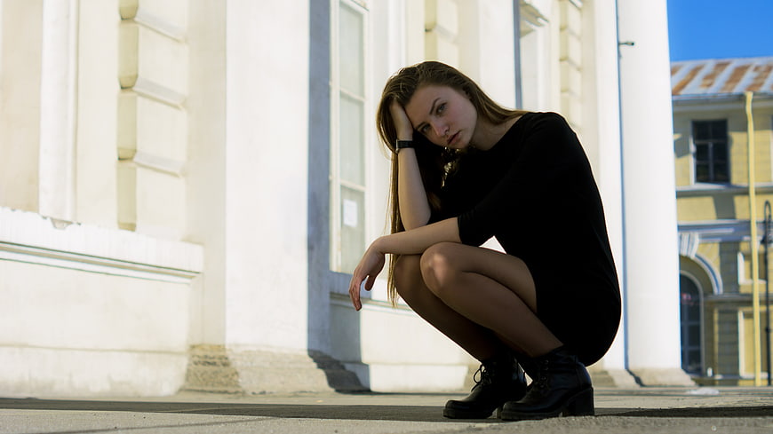 Sad young woman squatting alone on city street