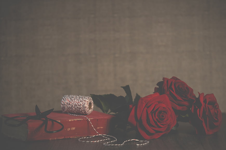 Vintage red roses and old book with scissors on wooden table