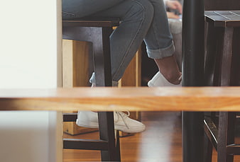 Close-up of white sneakers and jeans under a wooden table