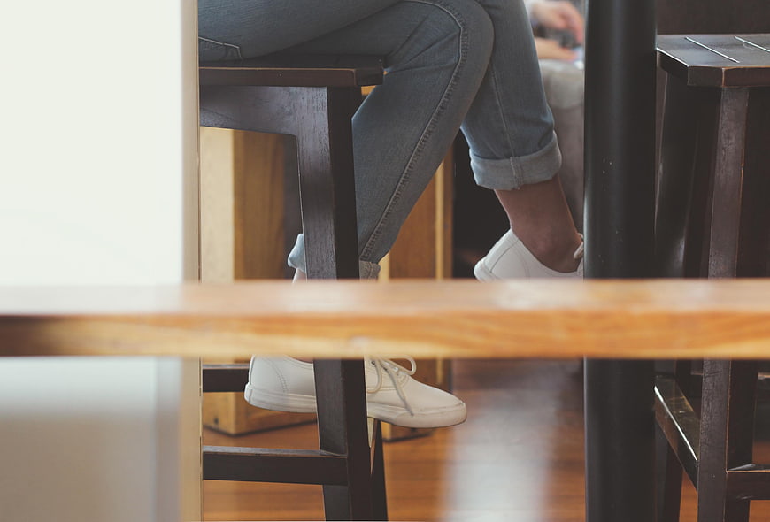 Close-up of white sneakers and jeans under a wooden table
