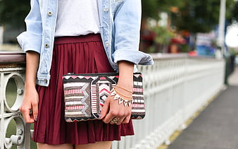 Woman holding patterned clutch purse with denim jacket