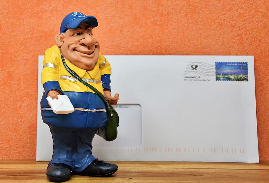 German Postman Figurine with Envelope on Wooden Surface
