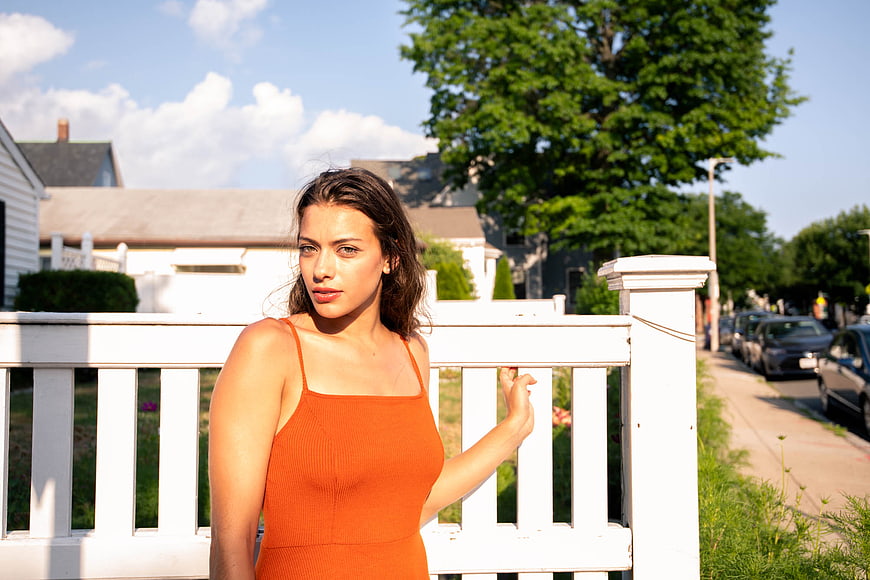 Young Woman in Orange Dress Standing by White Fence