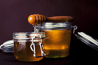 Glass Jars of Honey with Wooden Dipper on Dark Background