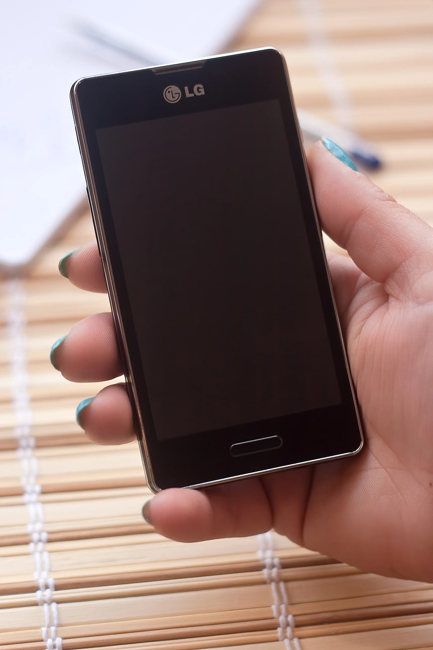 Hand Holding Black LG Smartphone on Bamboo Mat