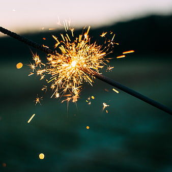 Close-up of burning sparkler with golden sparks against dark background