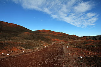 Red volcanic landscape with winding dirt road and blue sky