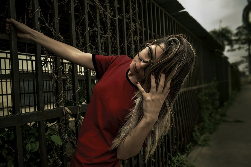 Woman in Red Shirt Leaning Against Metal Fence