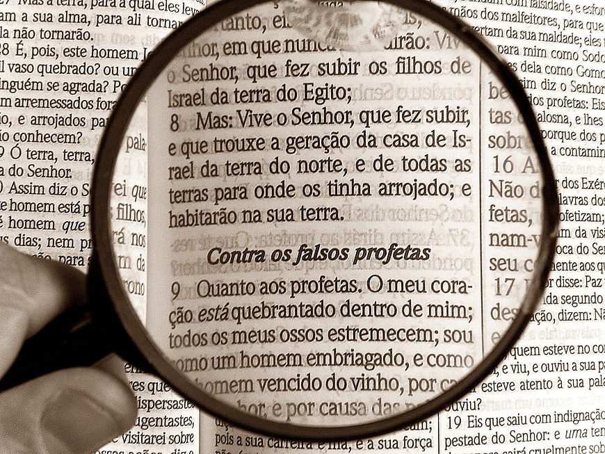 Magnifying glass focusing on Portuguese Bible text about false prophets