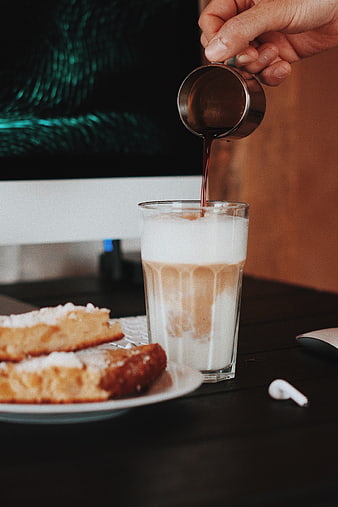 Pouring espresso into iced latte with pastry on desk
