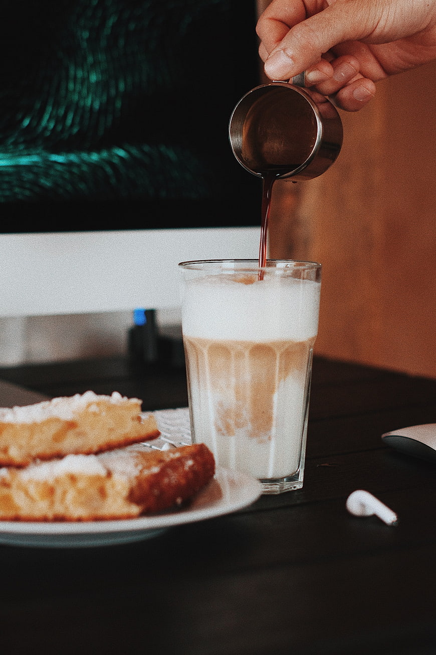 Pouring espresso into iced latte with pastry on desk