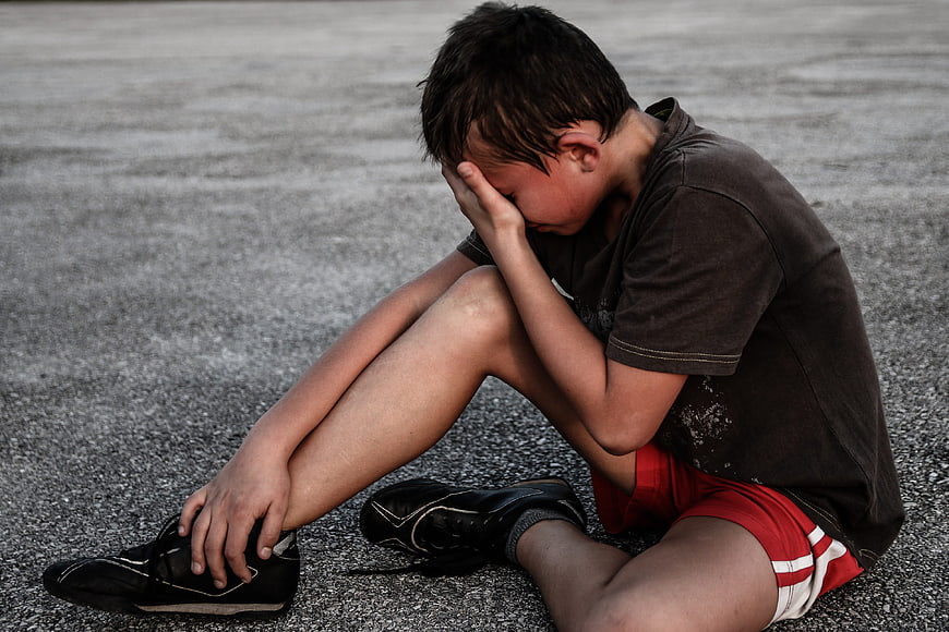Sad boy sitting on asphalt holding head in hands