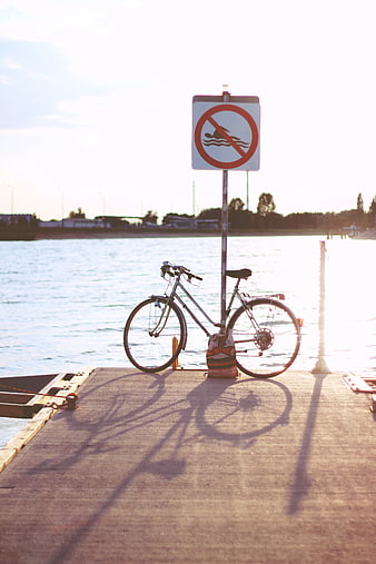 Bicycle parked on dock with no swimming sign at sunset