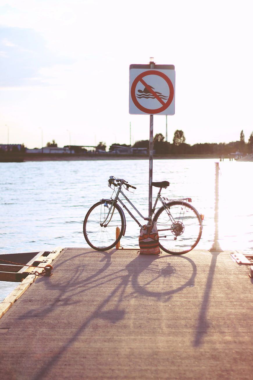 Bicycle parked on dock with no swimming sign at sunset