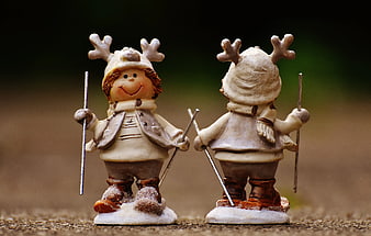 Two beige skiing figurines with reindeer antlers on snow base