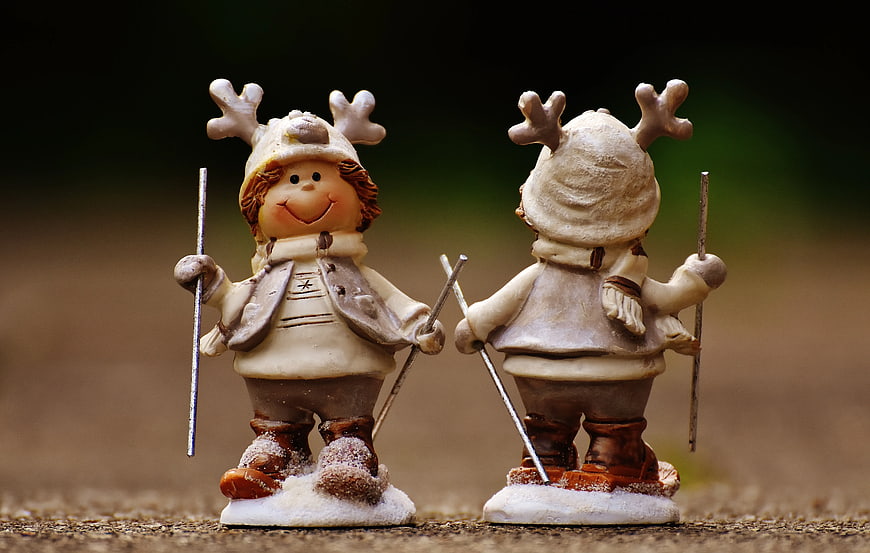 Two beige skiing figurines with reindeer antlers on snow base
