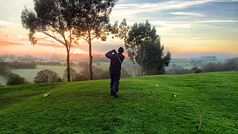 Golfer Swinging on Green Hillside at Sunset