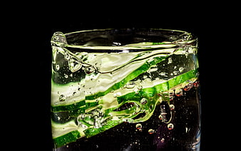 Refreshing cucumber slices in sparkling water glass on black background