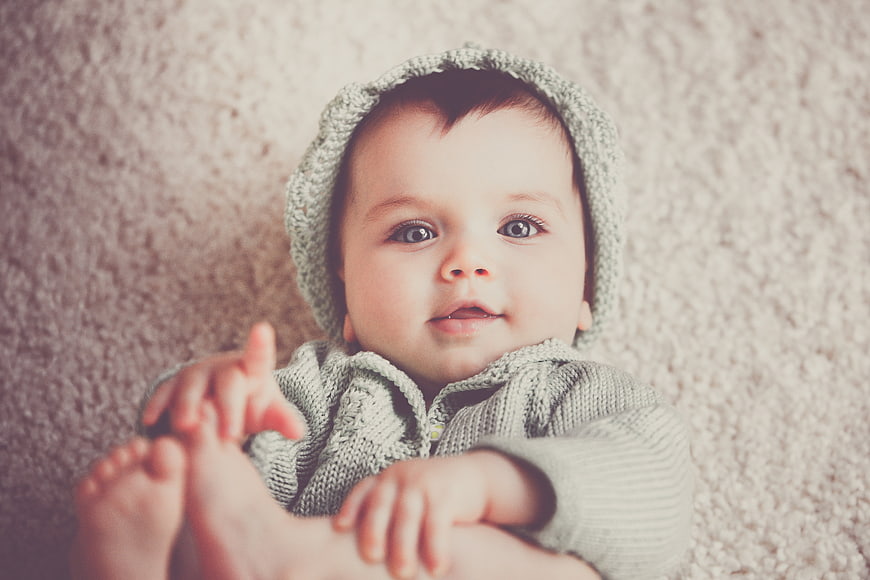 Cute baby in knitted hat lying on carpet