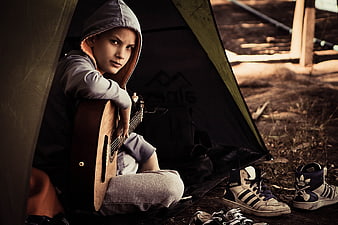 Boy with acoustic guitar sitting inside camping tent outdoors